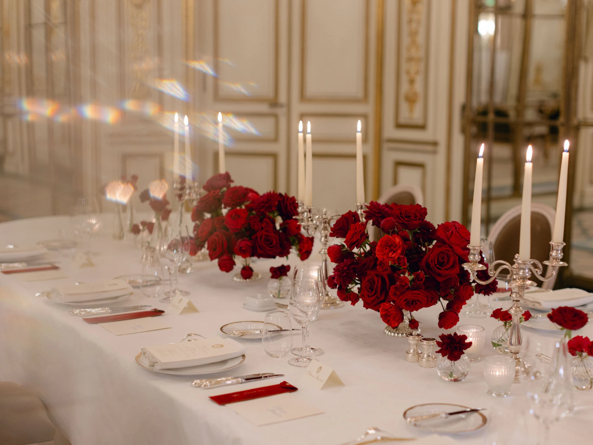 Elegant wedding banquet table with deep red roses, silver candelabras, crystal glassware and candlelight in a gilded Parisian salon